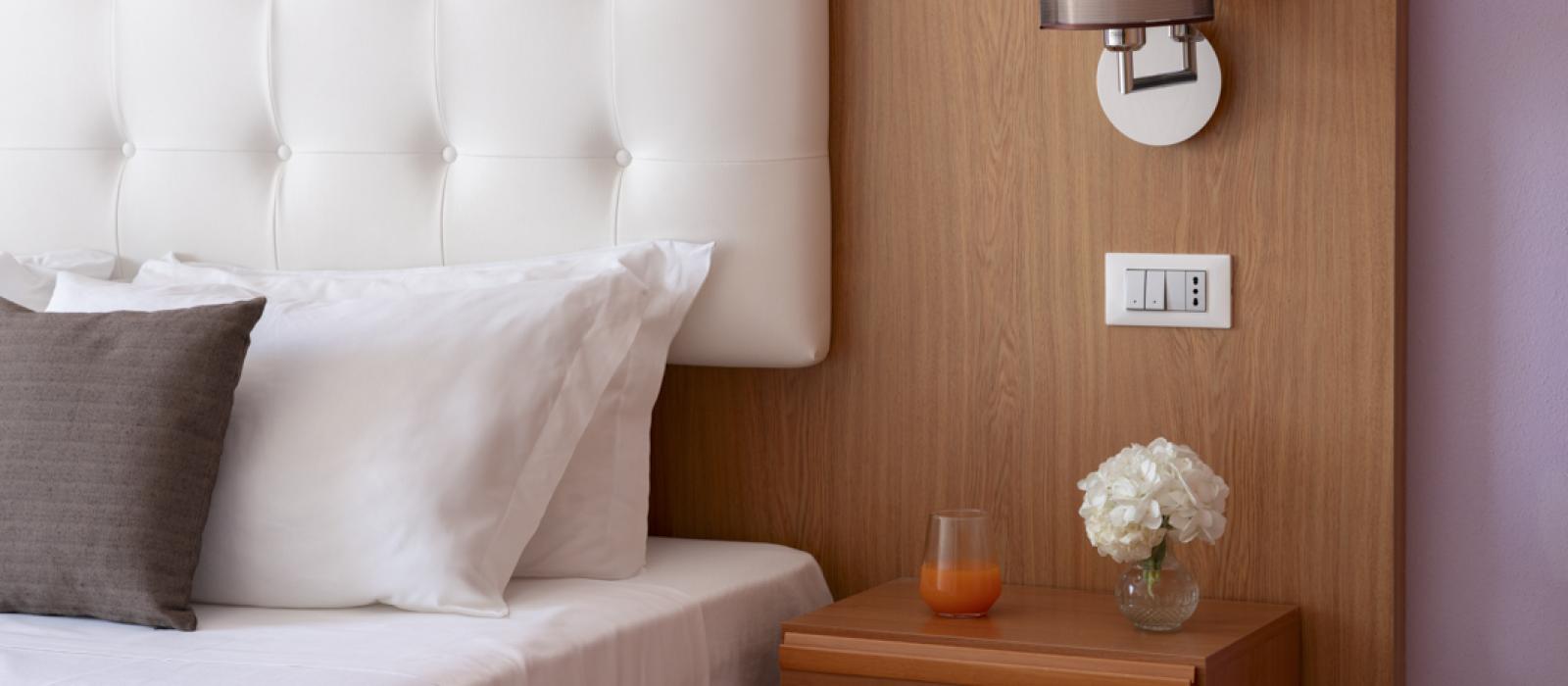 Camera da letto moderna con testiera bianca, lampada, e comodino con fiori e succo.