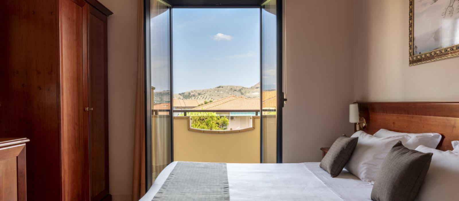 Camera d'albergo luminosa con letto matrimoniale, scrivania e balcone con vista.