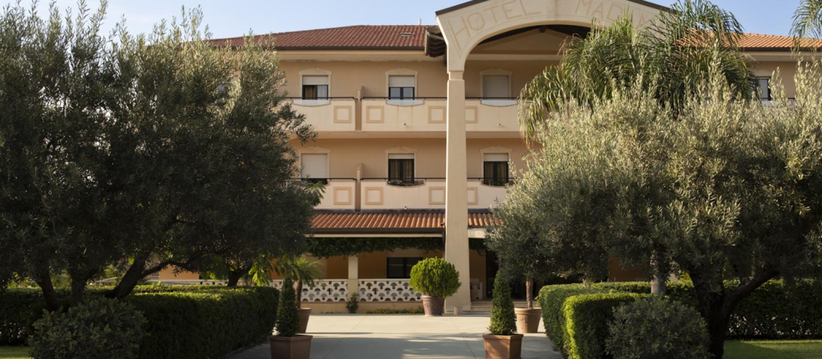 Edificio giallo con balconi, circondato da giardini verdi e fiori rossi.