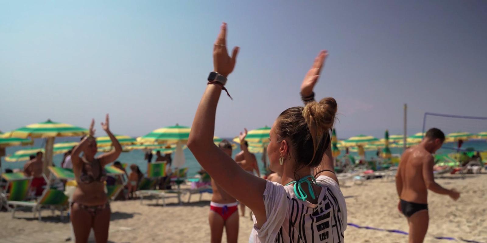Persone ballano sulla spiaggia sotto ombrelloni verdi e gialli.