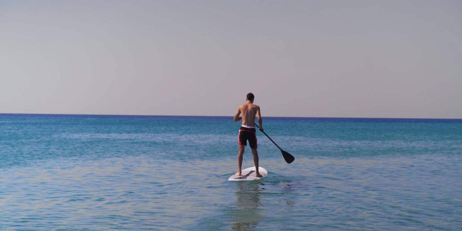 Persona fa paddleboarding in mare calmo sotto un cielo limpido.