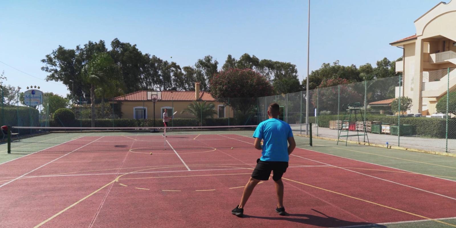 Due persone giocano a tennis su un campo all'aperto.