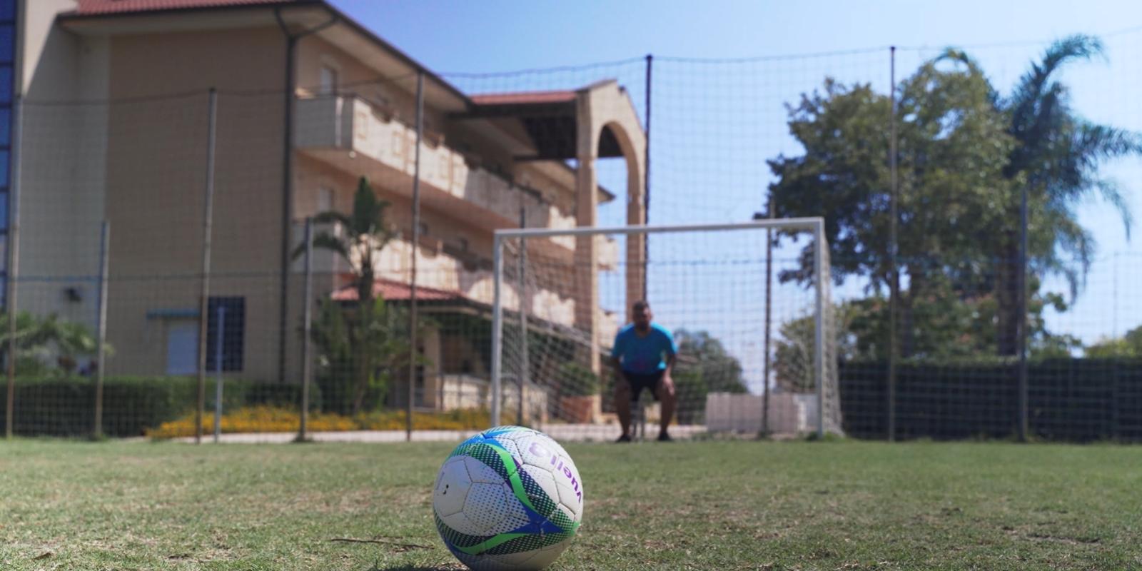 Pallone da calcio in primo piano, portiere in attesa davanti alla porta.