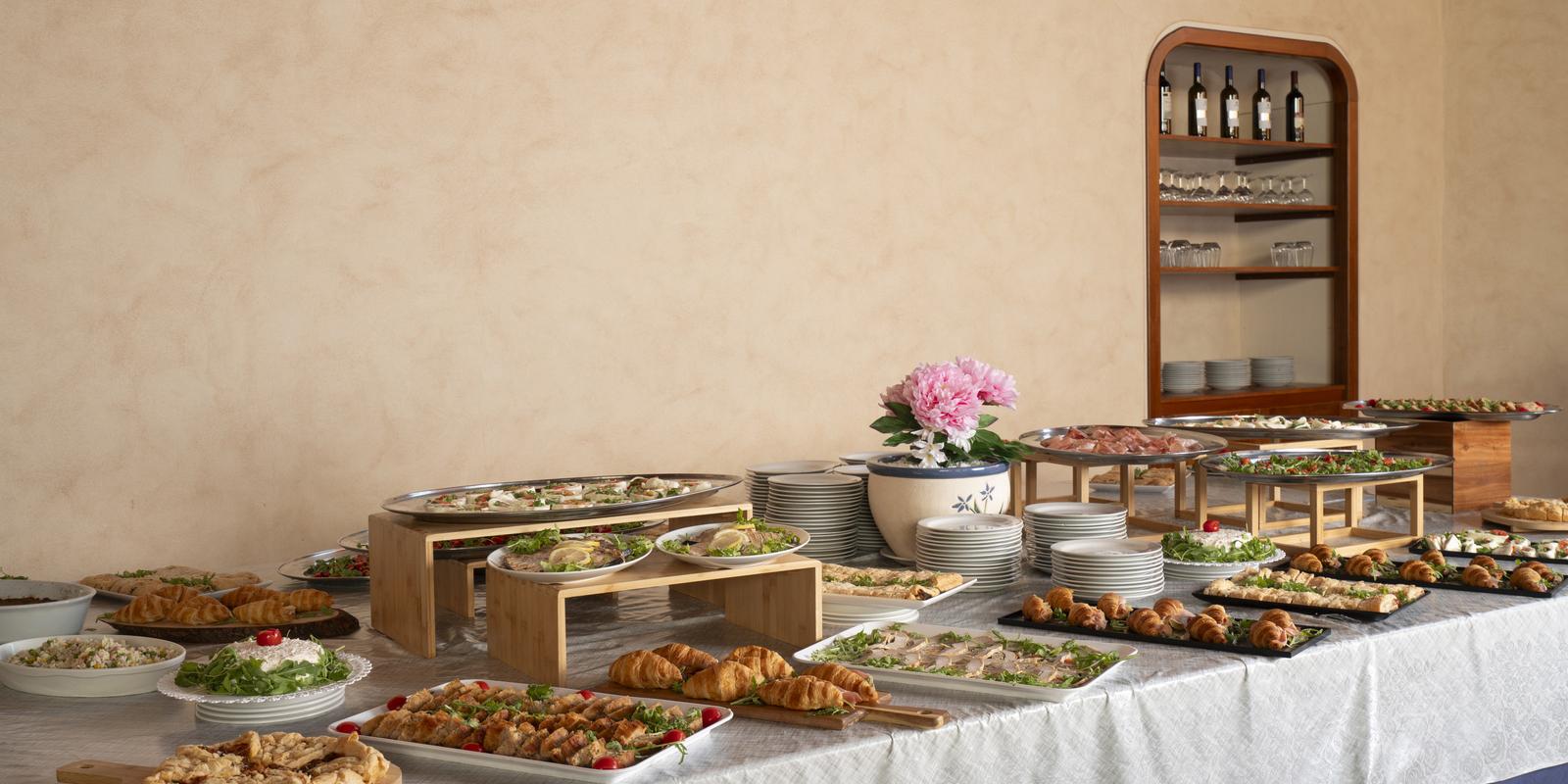 Buffet elegante con piatti assortiti, croissant, insalate e decorazioni floreali.