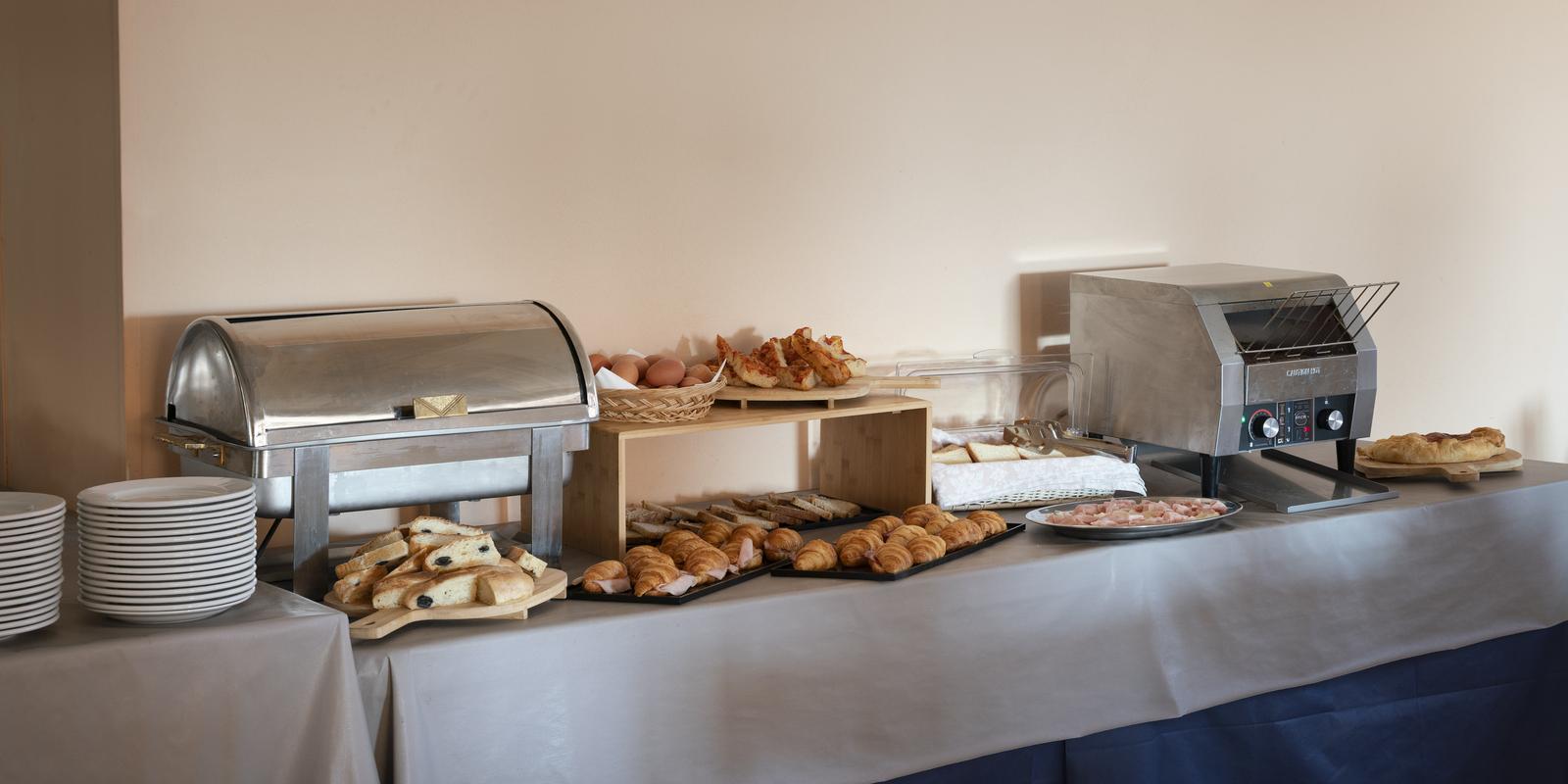 Buffet con croissant, pane, affettati, uova e macchina per toast.