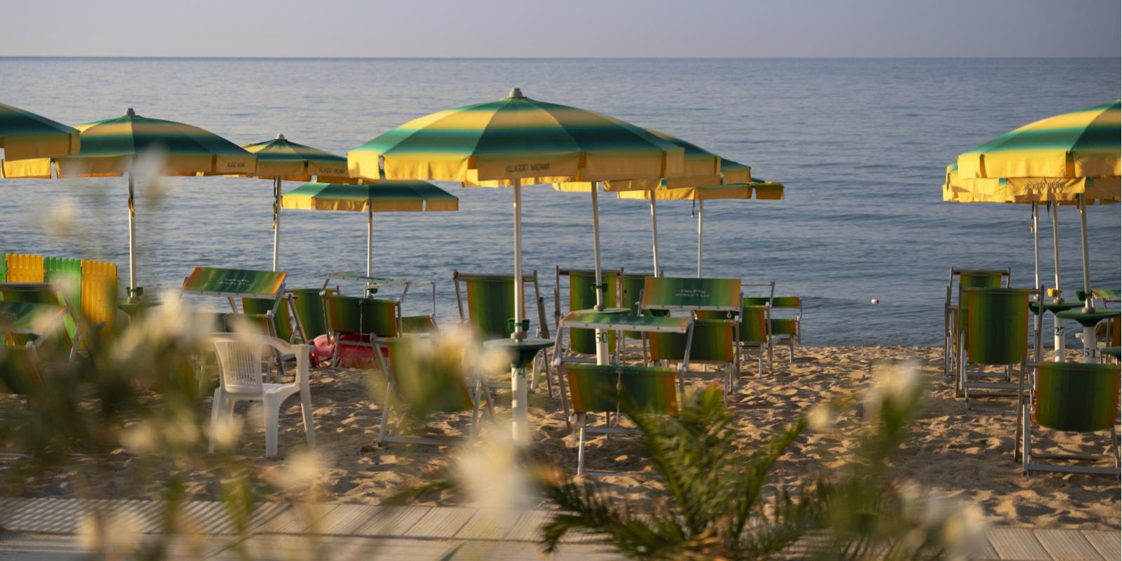 Spiaggia con ombrelloni e sedie a sdraio verdi e gialle, mare calmo sullo sfondo.