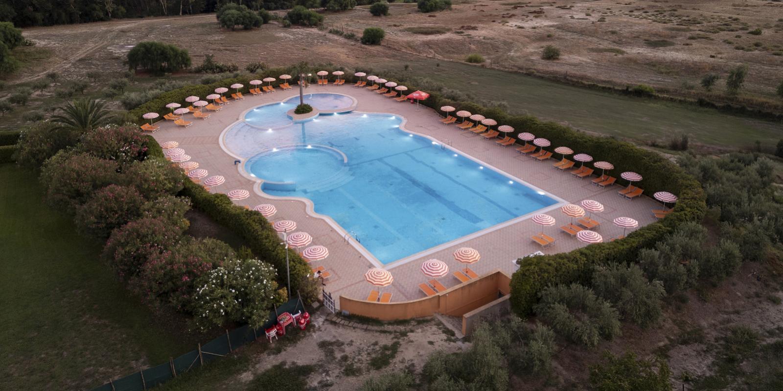 Piscina all'aperto circondata da ombrelloni e lettini, immersa nel verde.