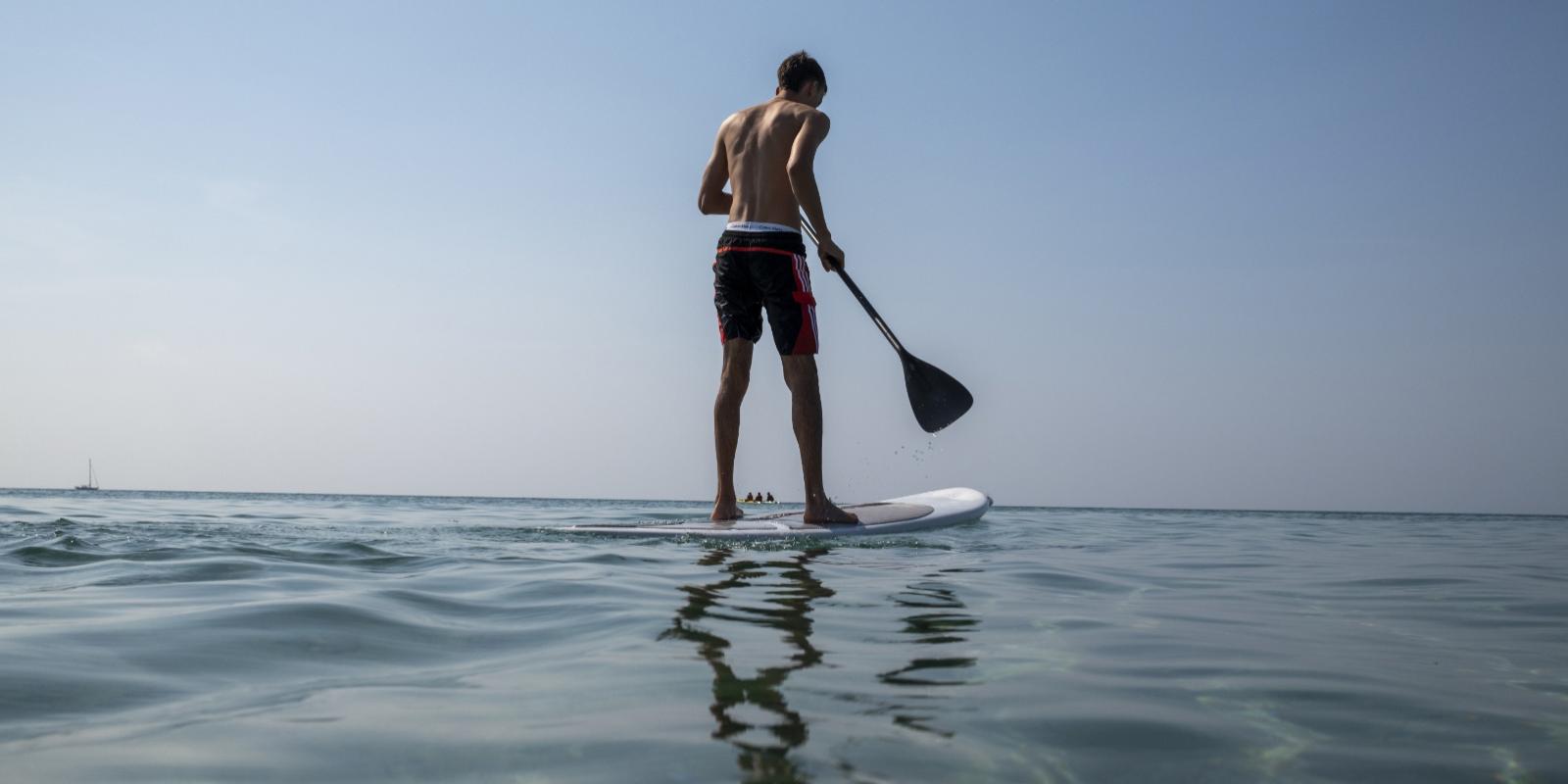 Persona fa paddleboarding in mare calmo sotto un cielo sereno.