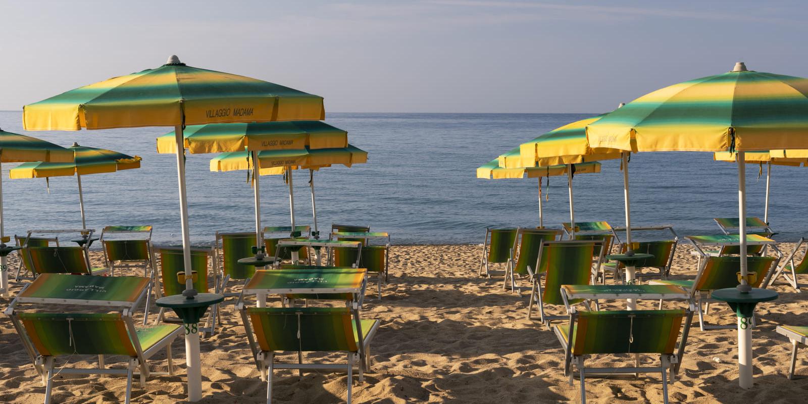 Spiaggia con ombrelloni e lettini verdi e gialli, mare calmo sullo sfondo.