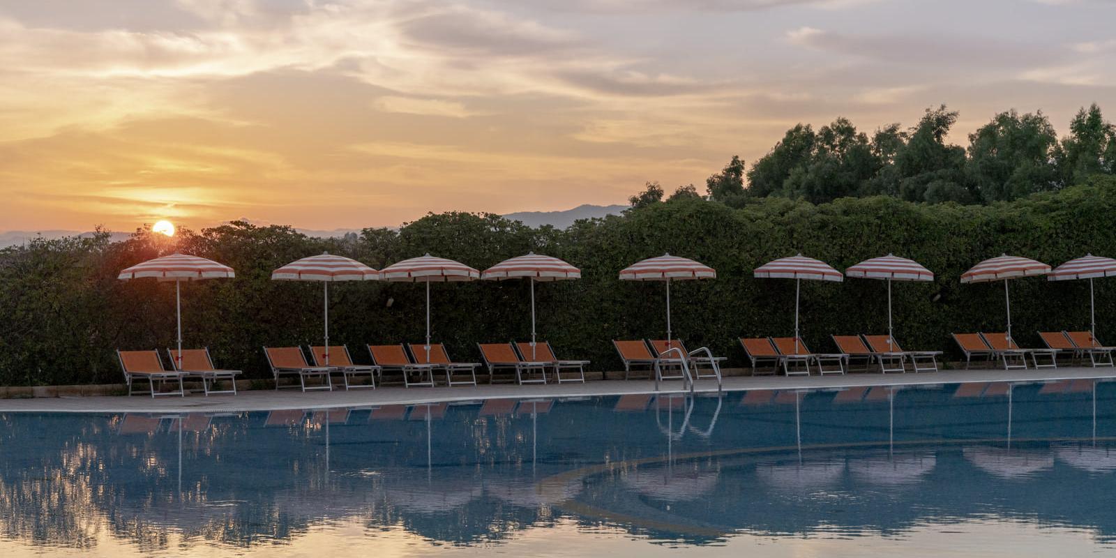 Piscina al tramonto con lettini e ombrelloni arancioni, atmosfera tranquilla e rilassante.
