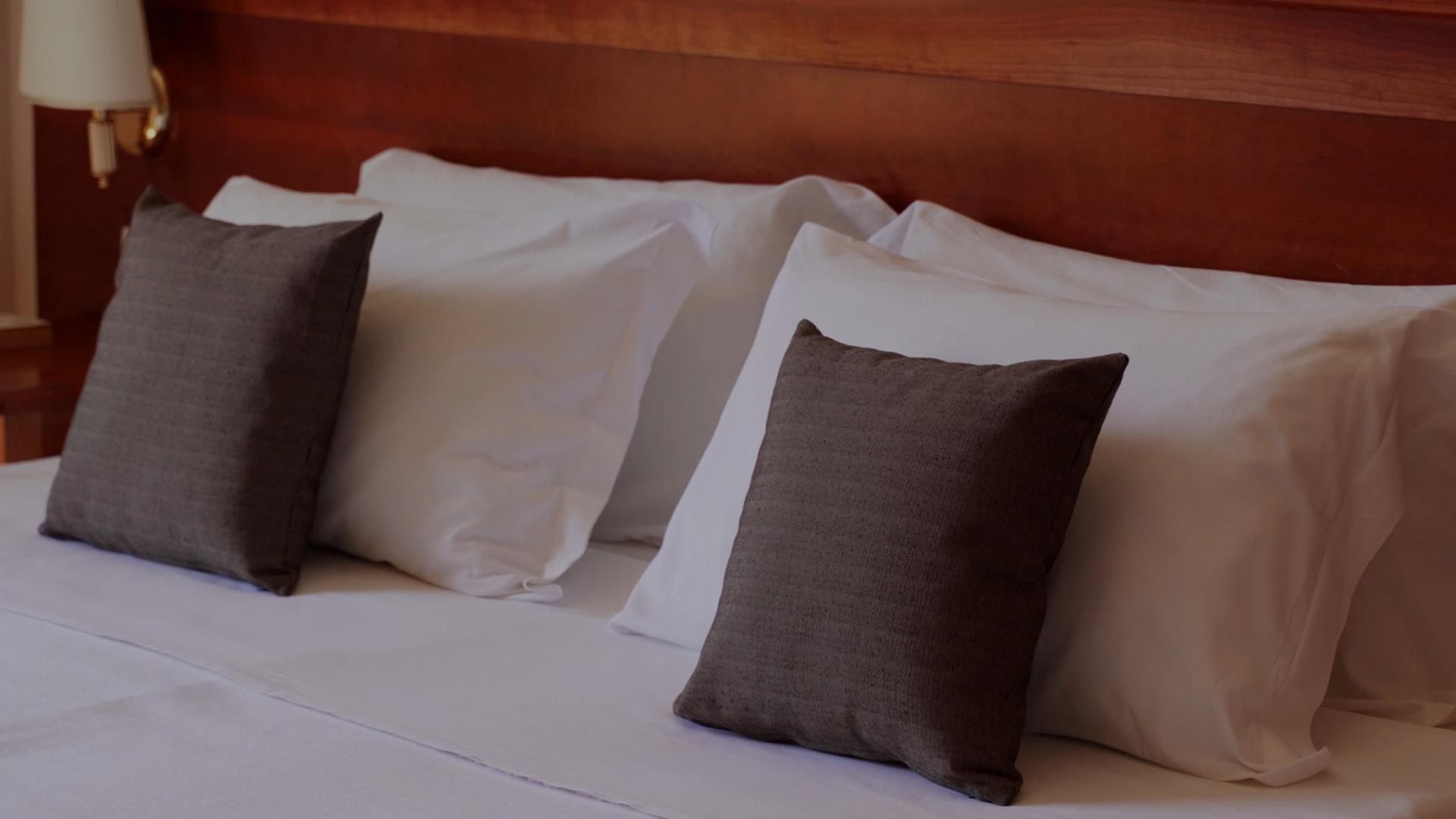 Letto con cuscini bianchi e cuscini decorativi scuri, testiera in legno.