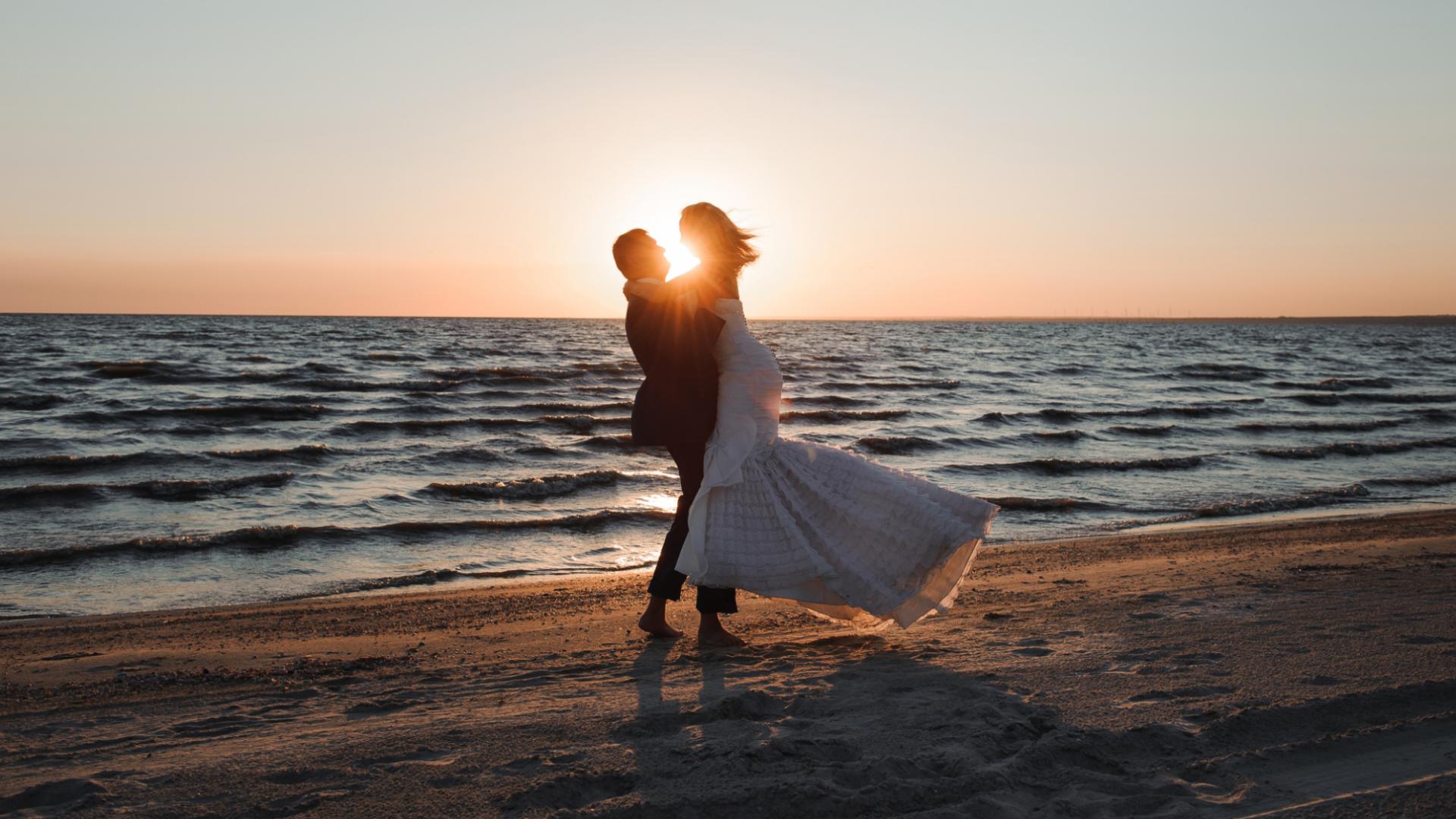 Una coppia abbracciata al tramonto su una spiaggia, con il sole all'orizzonte.