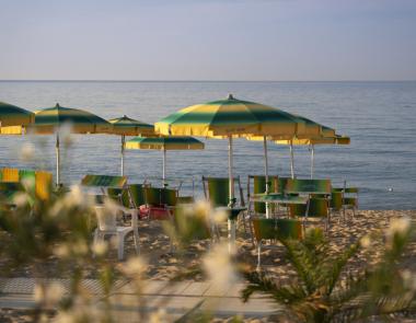 Spiaggia con ombrelloni gialli e verdi, sedie e mare calmo.