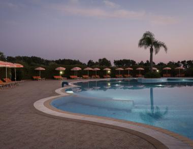 Piscina all'aperto al tramonto, con lettini e ombrelloni arancioni e palme.