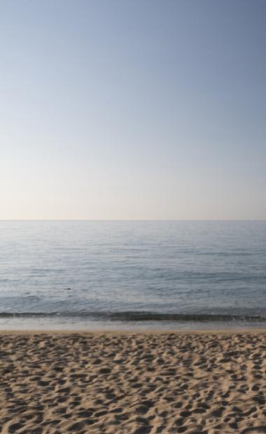 Spiaggia sabbiosa con mare calmo al tramonto sotto un cielo limpido.