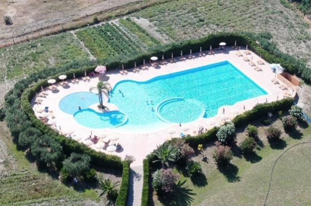 Piscina all'aperto circondata da vegetazione e ombrelloni in un'area rurale.