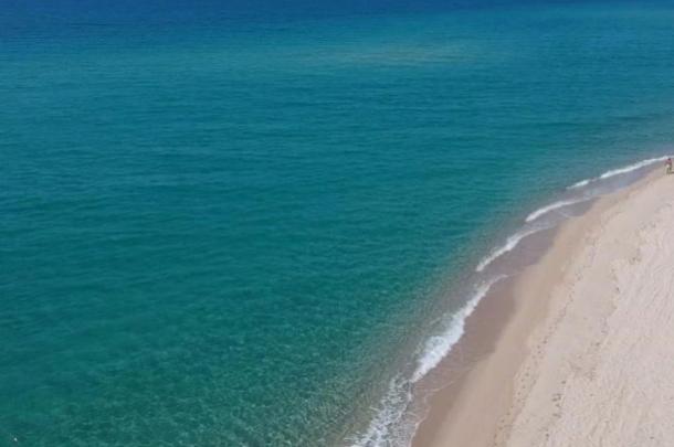 Spiaggia di sabbia bianca con mare turchese e onde leggere.