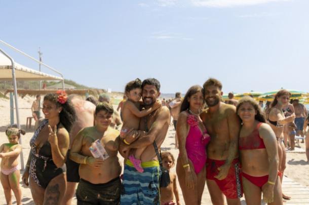 Gruppo di persone sorridenti in spiaggia durante una giornata di sole.