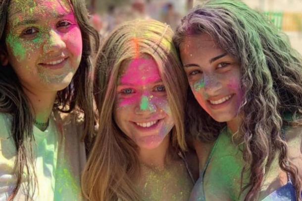 Tre ragazze sorridenti coperte di colori vivaci durante una festa.