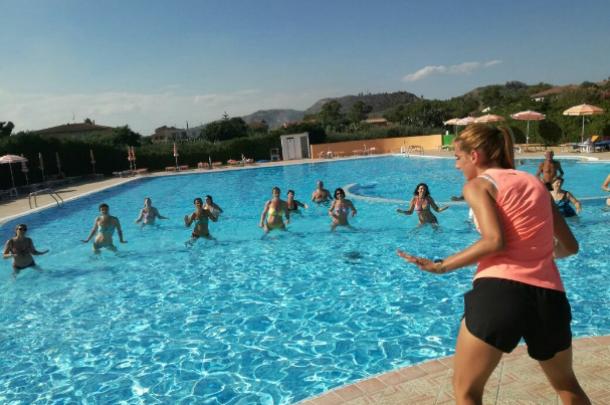 Lezione di acquagym in piscina con istruttrice e partecipanti sotto il sole estivo.