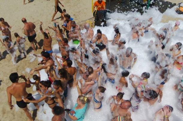 Persone si divertono in una festa di schiuma sulla spiaggia.