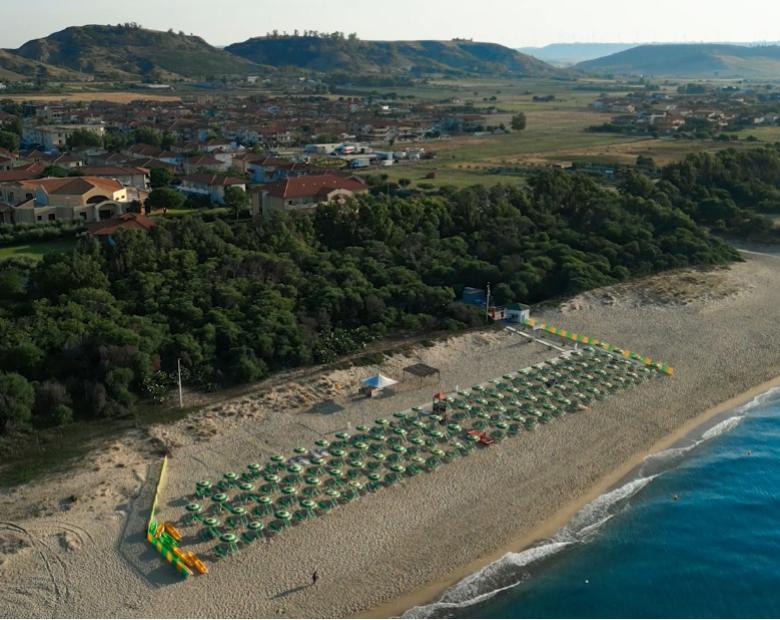 Spiaggia con ombrelloni verdi, mare blu e case sullo sfondo.