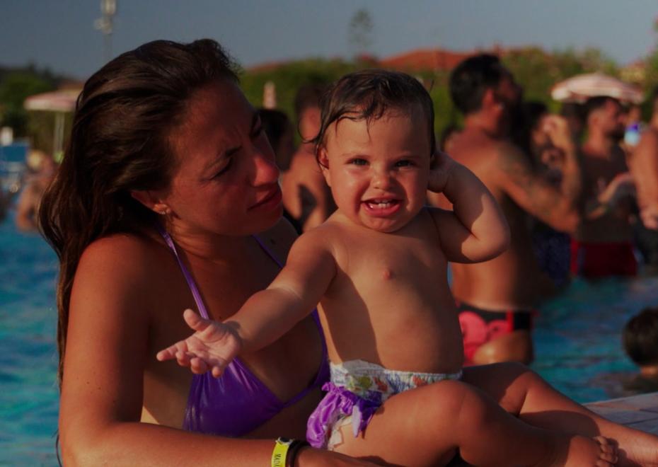 Una donna e un bambino sorridente in piscina, circondati da altre persone.