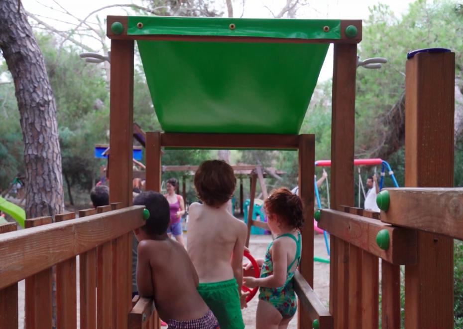 Bambini giocano su una struttura in legno in un parco giochi immerso nel verde.