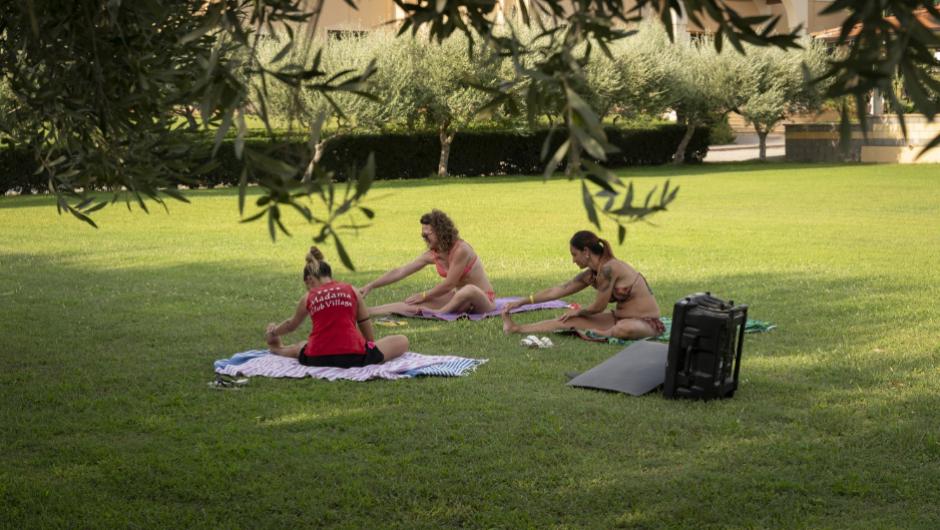 Tre persone fanno yoga su un prato verde in un ambiente rilassante.