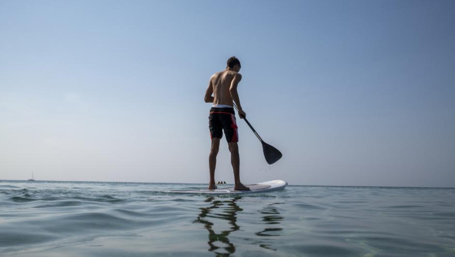 Persona fa paddleboarding su mare calmo sotto un cielo azzurro.