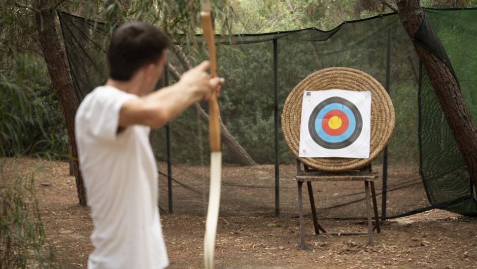 Persona che pratica tiro con l'arco in un'area all'aperto con bersaglio.