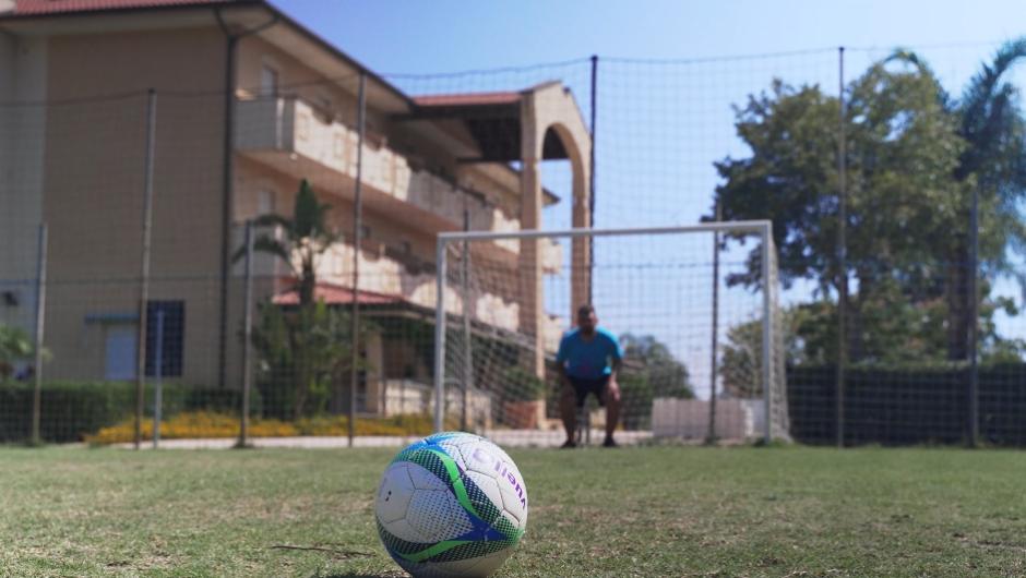 Pallone da calcio in primo piano, portiere in attesa davanti alla porta.