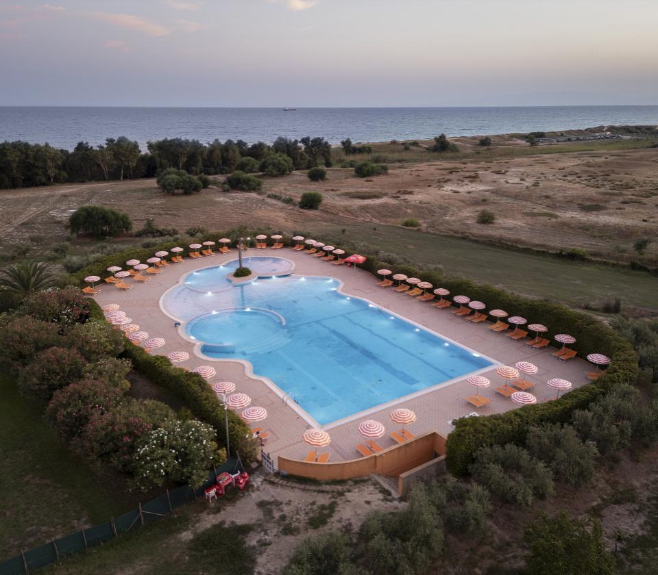 Piscina all'aperto con ombrelloni, vista mare e paesaggio naturale circostante.