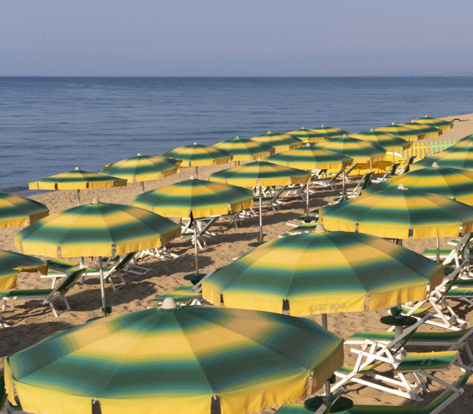 Spiaggia con ombrelloni gialli e verdi, mare calmo e sabbia dorata.